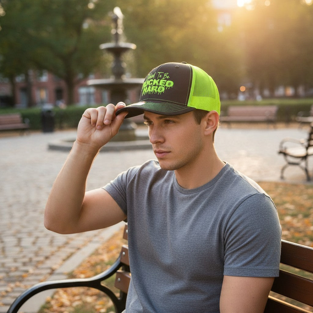 Dirty Merch Apparel trucker hat in charcoal and neon green with graphic embroidery worn by a man in a park.