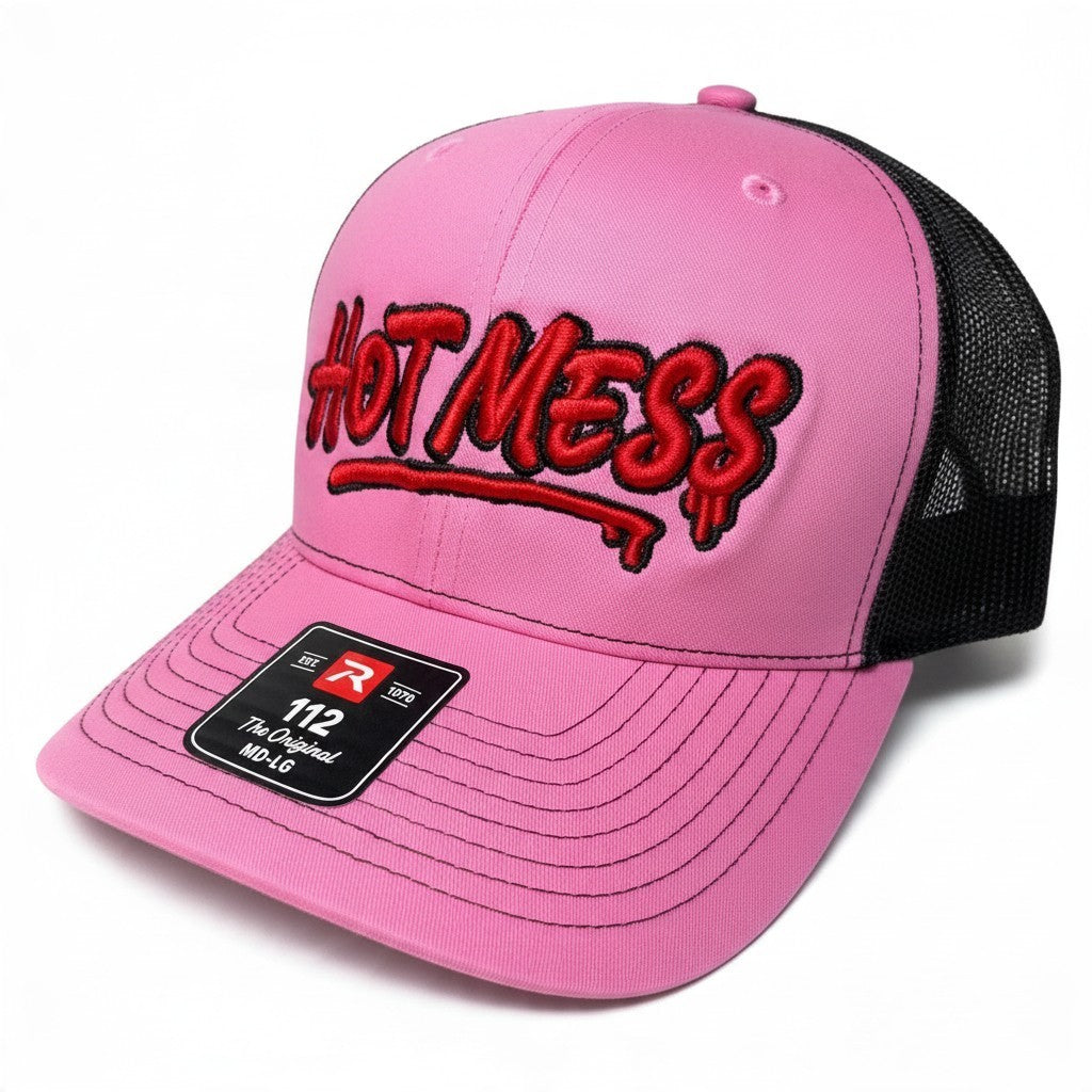 Dirty Merch Apparel pink trucker hat with black mesh back and red graffiti-style HOT MESS embroidery on front panel.