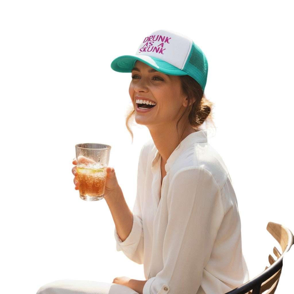 Dirty Merch Apparel teal and white mesh trucker hat with Drunk As A Skunk embroidery worn by a smiling woman